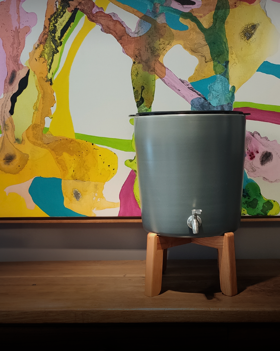 Purificador Acqualive Terracota em versão grafite com arte contemporânea ao fundo, design para mulheres maduras